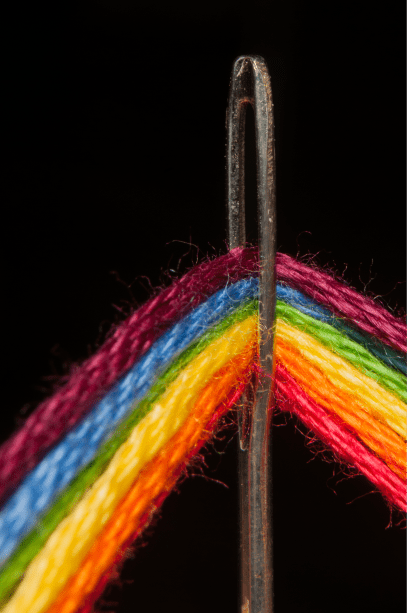 Image of rainbow colored thread going through the eye of a needle